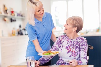 smiling senior woman in wheelchair is served breakfast by her caregiver