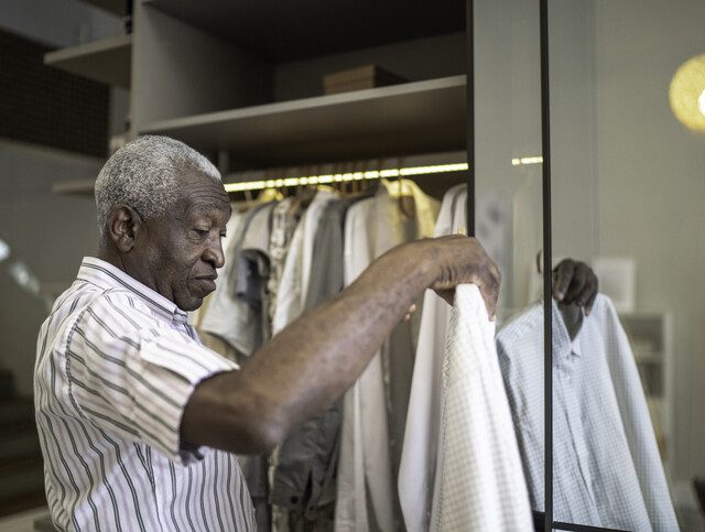 senior man holds button-up shirt and prepares to hang it in his closet