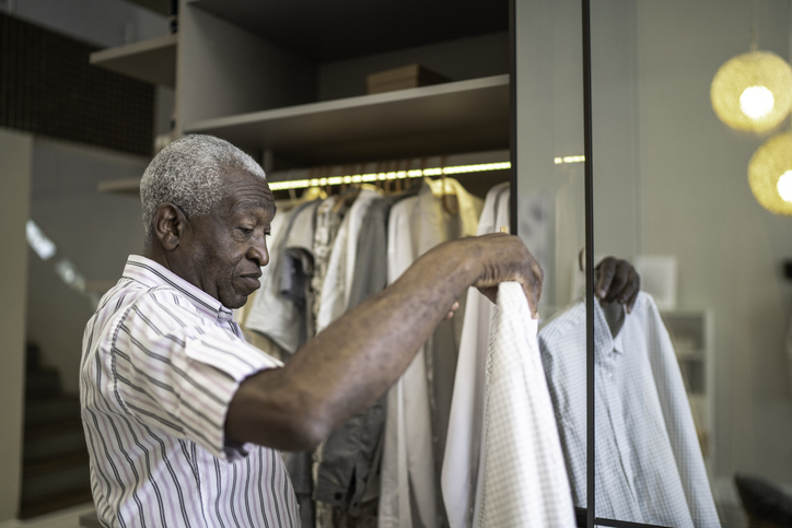 senior man holds button-up shirt and prepares to hang it in his closet