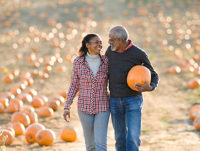 senior couple smile while walking through a field of pumpkins after selecting the perfect one