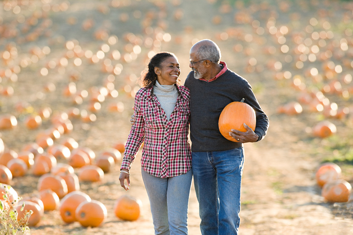 senior couple smile while walking through a field of pumpkins after selecting the perfect one