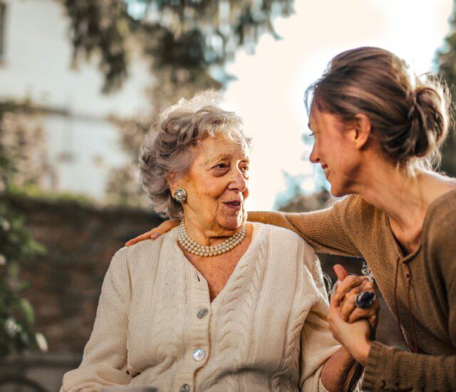 senior woman and her adult daughter speak happily while seated outdoors