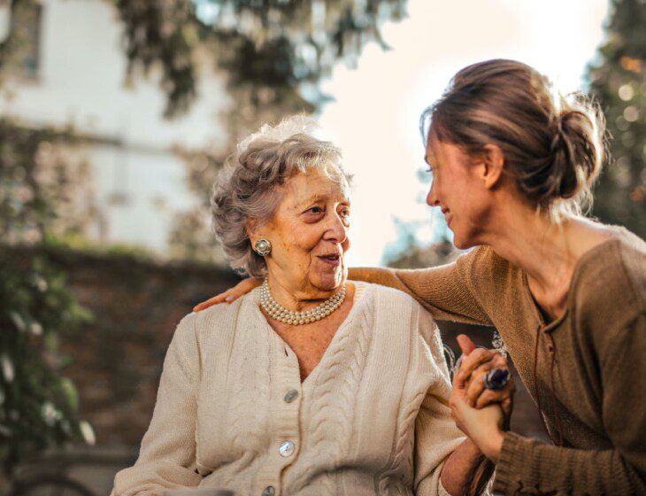 senior woman and her adult daughter speak happily while seated outdoors