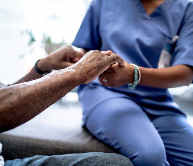 seated senior man holds the hands of a nurse at his senior living community