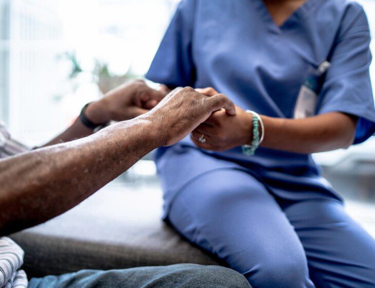 seated senior man holds the hands of a nurse at his senior living community