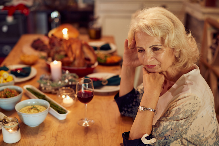 senior woman sits alone at a table set for Thanksgiving, looking forlorn