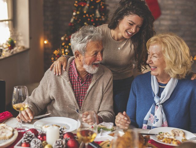 senior couple and their adult daughter smile while enjoying Christmas dinner together
