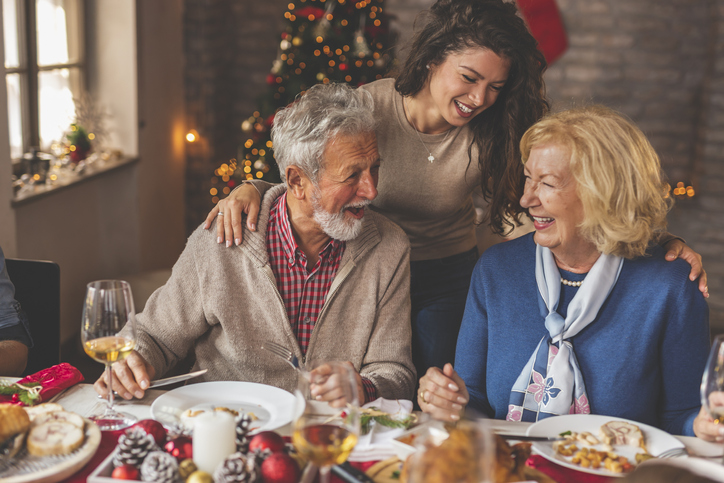 senior couple and their adult daughter smile while enjoying Christmas dinner together