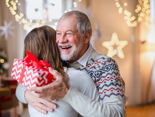 senior man smiles while hugging his adult daughter, holding a gift he received from her