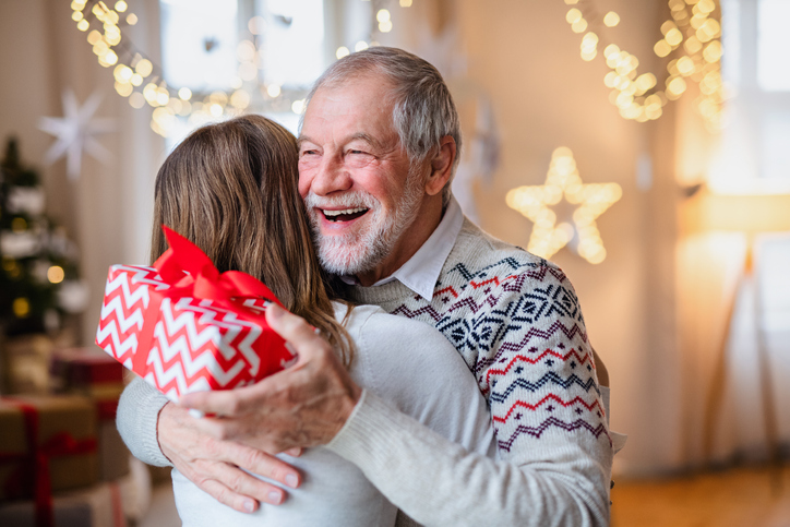 senior man smiles while hugging his adult daughter, holding a gift he received from her