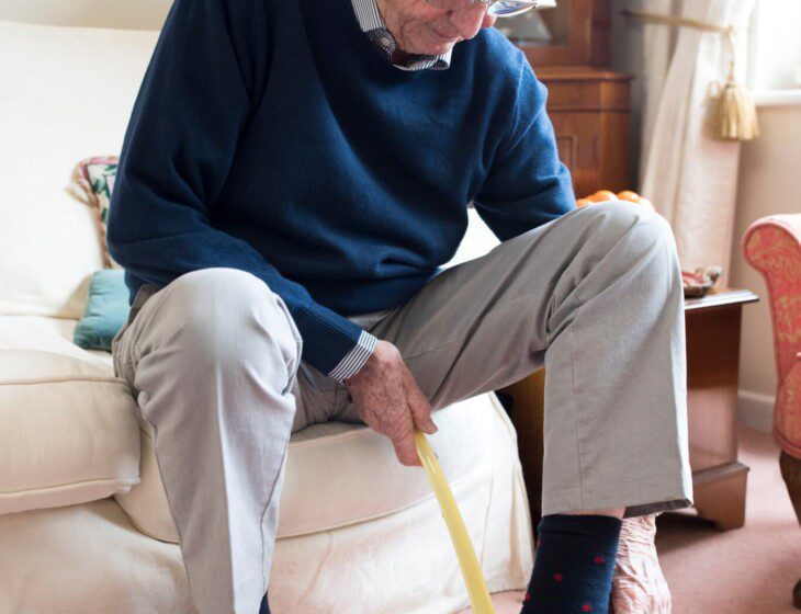 well-dressed senior man using shoe horn to put on his dress shoes while seated