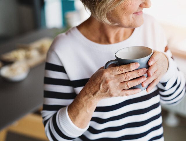 close-up of senior woman in striped shirt holding coffee mug