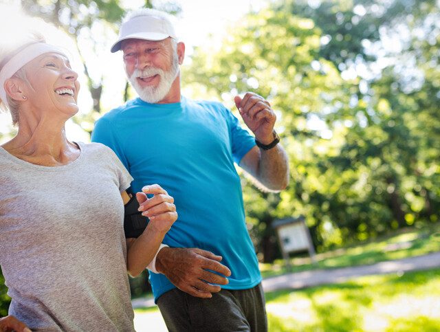 senior couple in athletic clothing smile while on a jog together outdoors