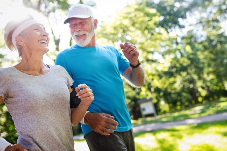 senior couple in athletic clothing smile while on a jog together outdoors