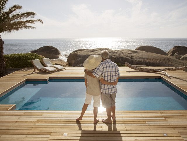 two older adults standing in front of pool overlooking beach