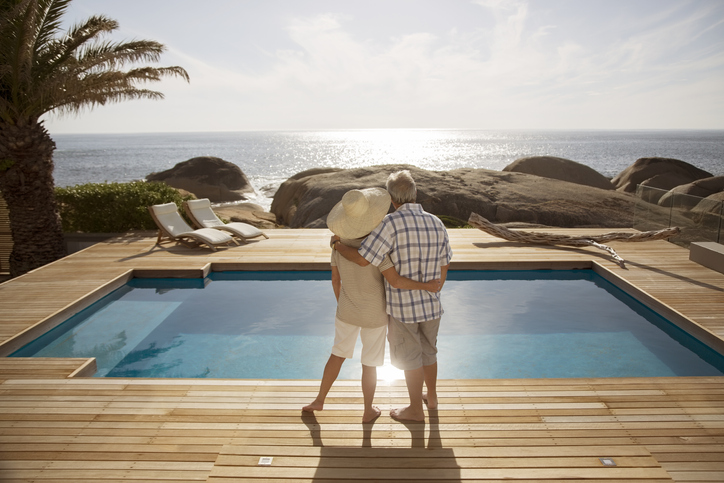 two older adults standing in front of pool overlooking beach